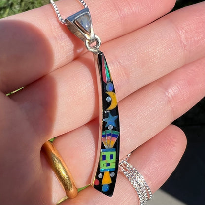 Angled close-up of imported Southwest-style sterling silver stone inlay pendant held in hand in sunlight.