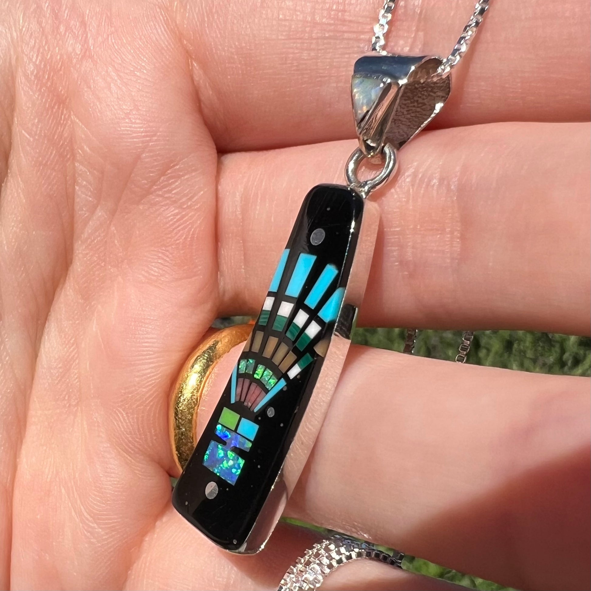 Close-up angled view of opal and onyx inlay necklace with Southwest-style design, held in hand under natural light.