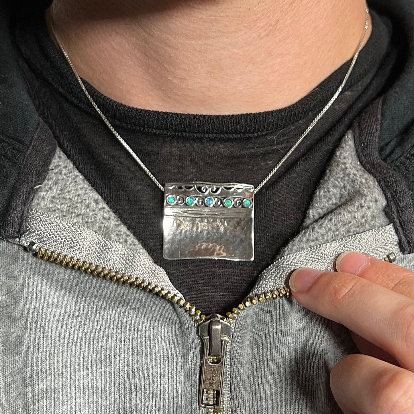 A handmade silver five-stone opal necklace with a hammered finish worn around a neck against a dark shirt.