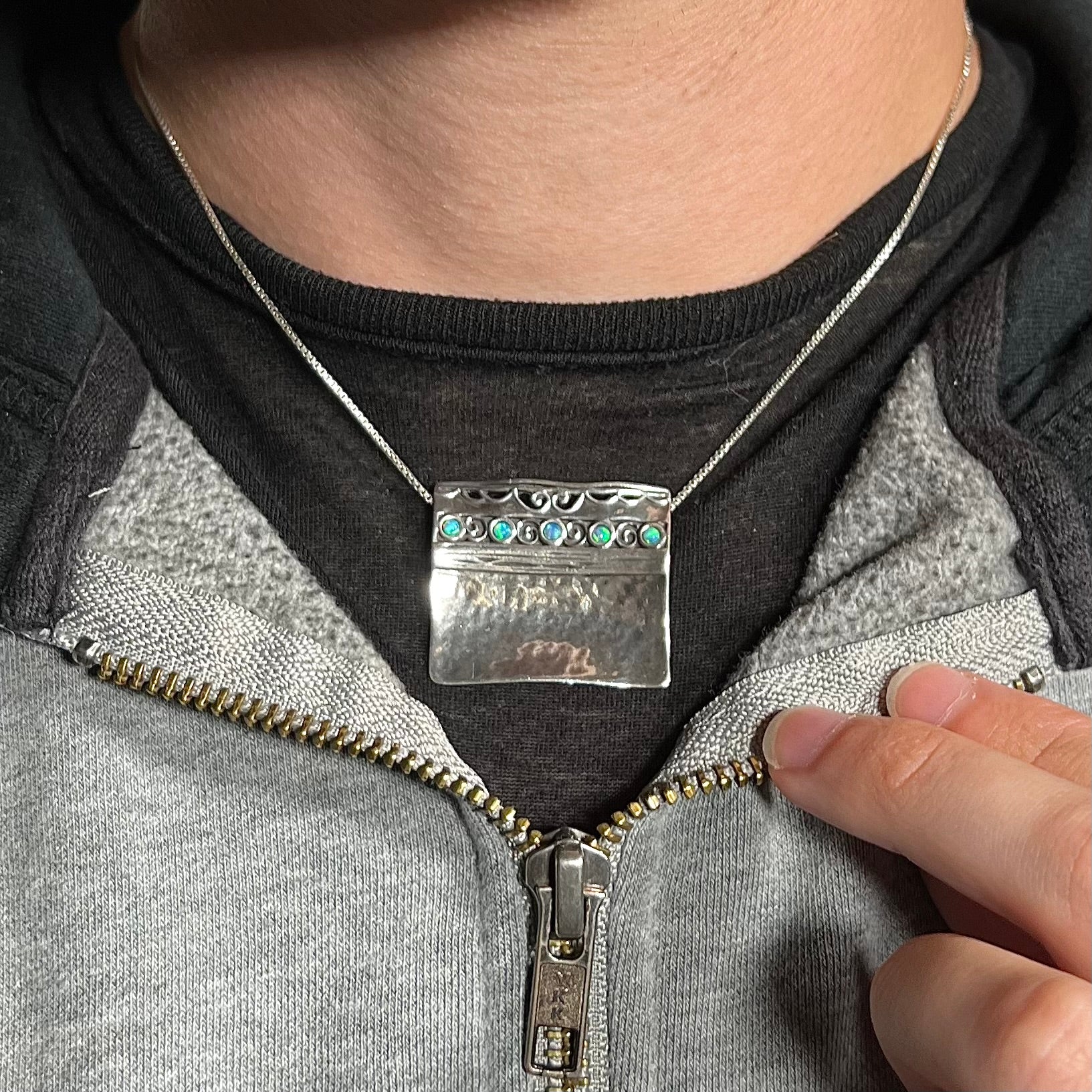 A handmade silver five-stone opal necklace with a hammered finish worn around a neck against a dark shirt.