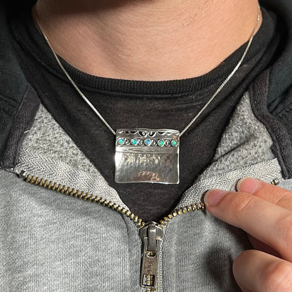 A handmade silver five-stone opal necklace with a hammered finish worn around a neck against a dark shirt.