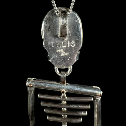 Back side of silver skeleton pendant showing hallmark stamps, "THEIS", "14K", and "STERLING", denoting Philadelphia artist, Jane Theis of HighArt