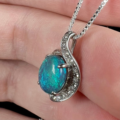 Close-up side view of an estate Japanese platinum pendant set with an Australian black opal and diamond accents, held in a hand.