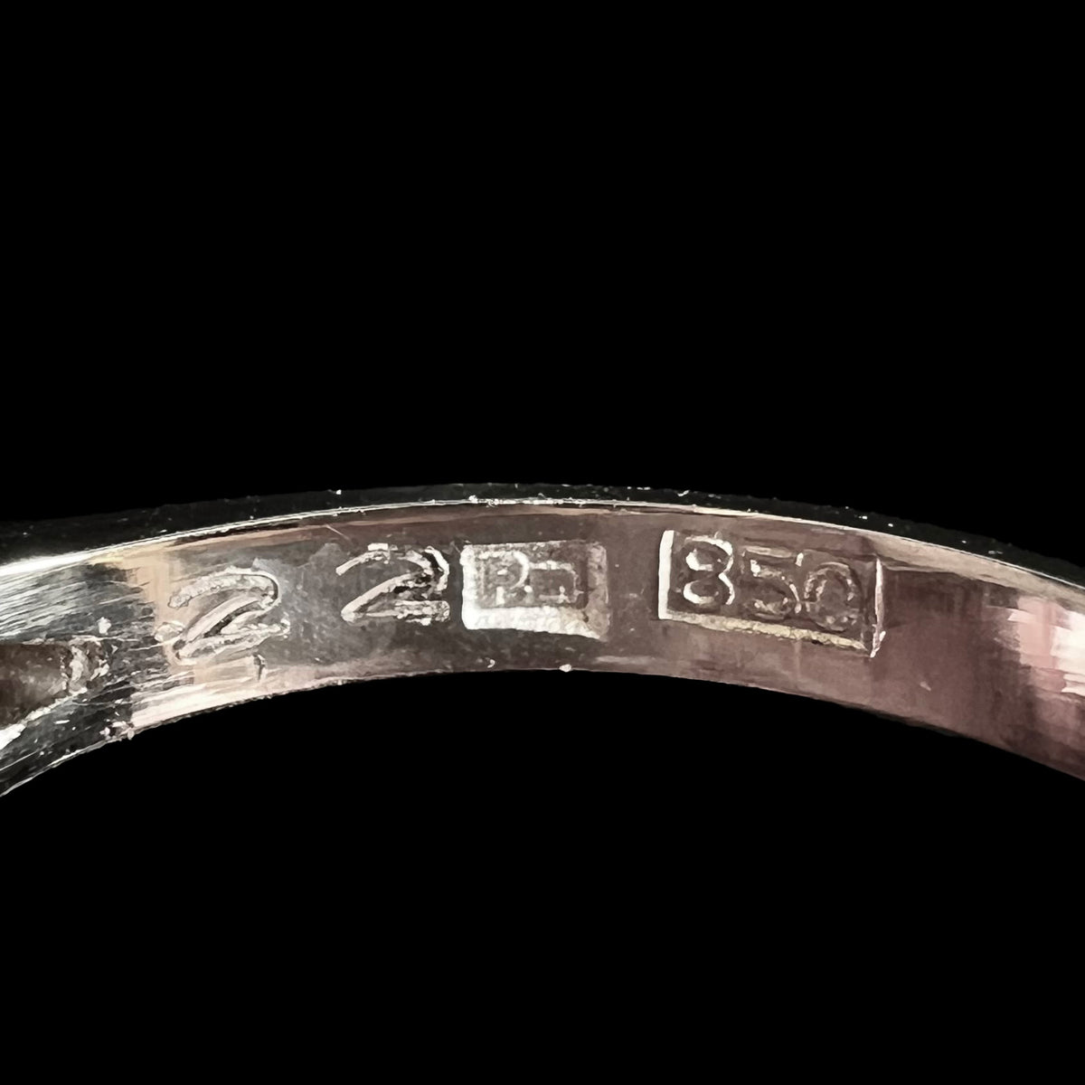 Macro view of inside of vintage Japanese platinum opal ring's shank, the hallmark stamps "22", "Pm", and "850" in focus.