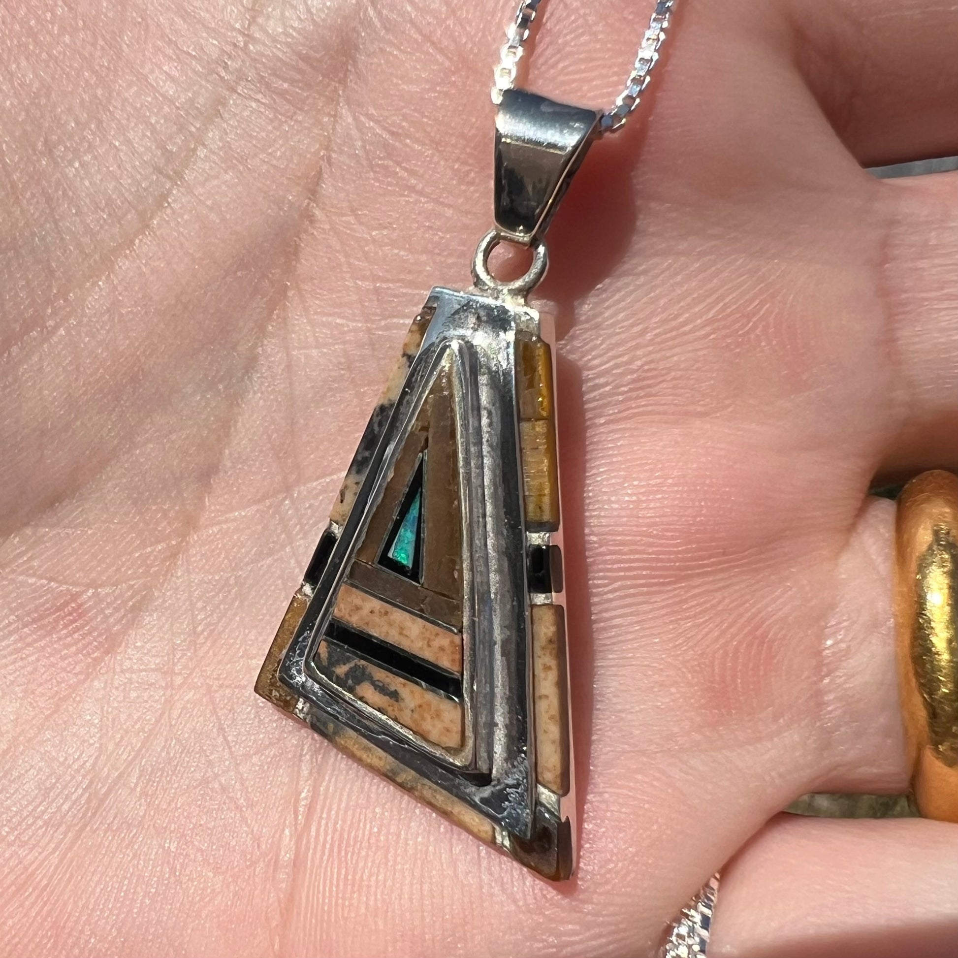 A sterling silver Australian opal, picture jasper, and onyx inlay pendant shown in sunlight close-up from an angle.