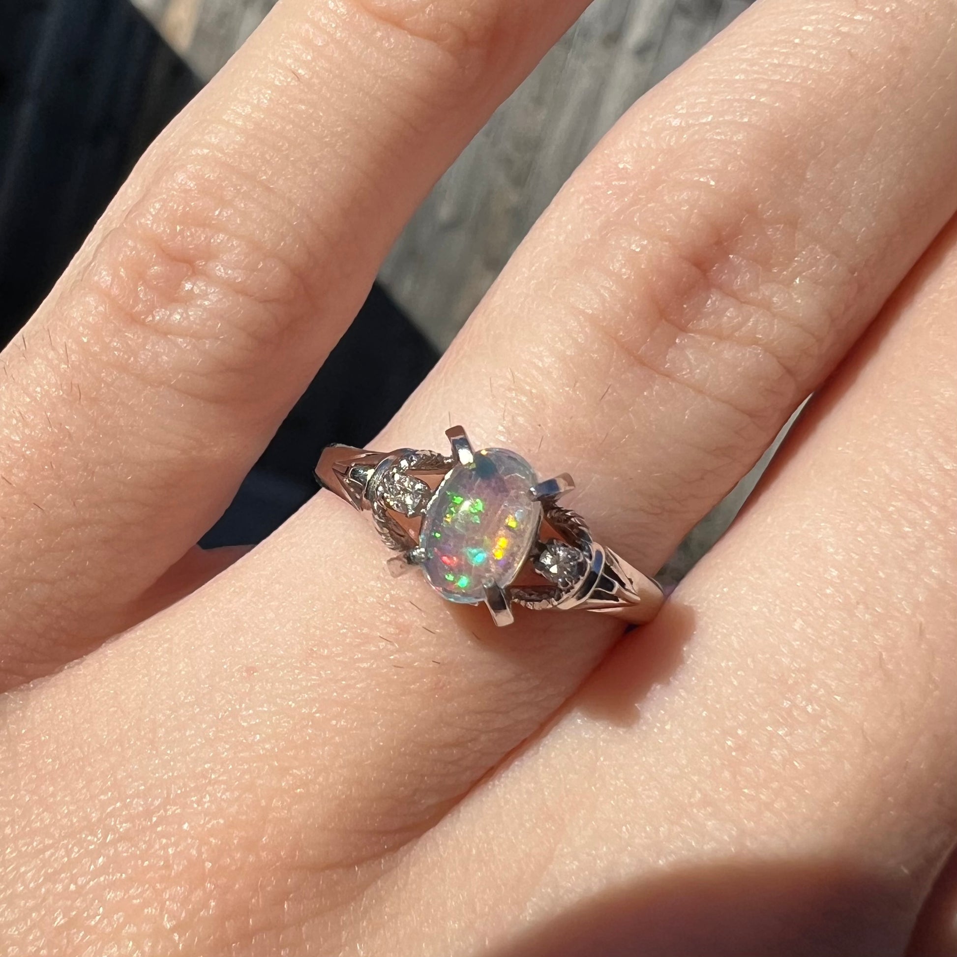 A dainty platinum jelly opal ring with diamonds worn on a finger in natural sunlight.