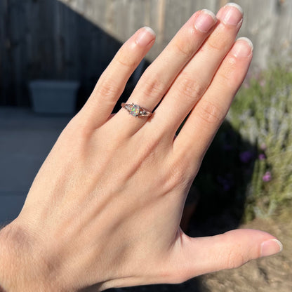 A dainty platinum jelly opal ring with diamonds worn on a hand in natural sunlight.