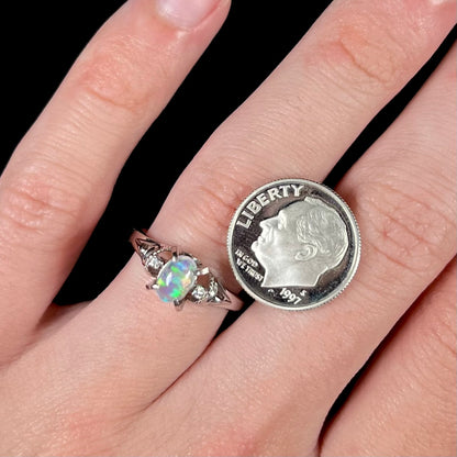 A delicate jelly opal and diamond engagement ring next to a US dime coin.