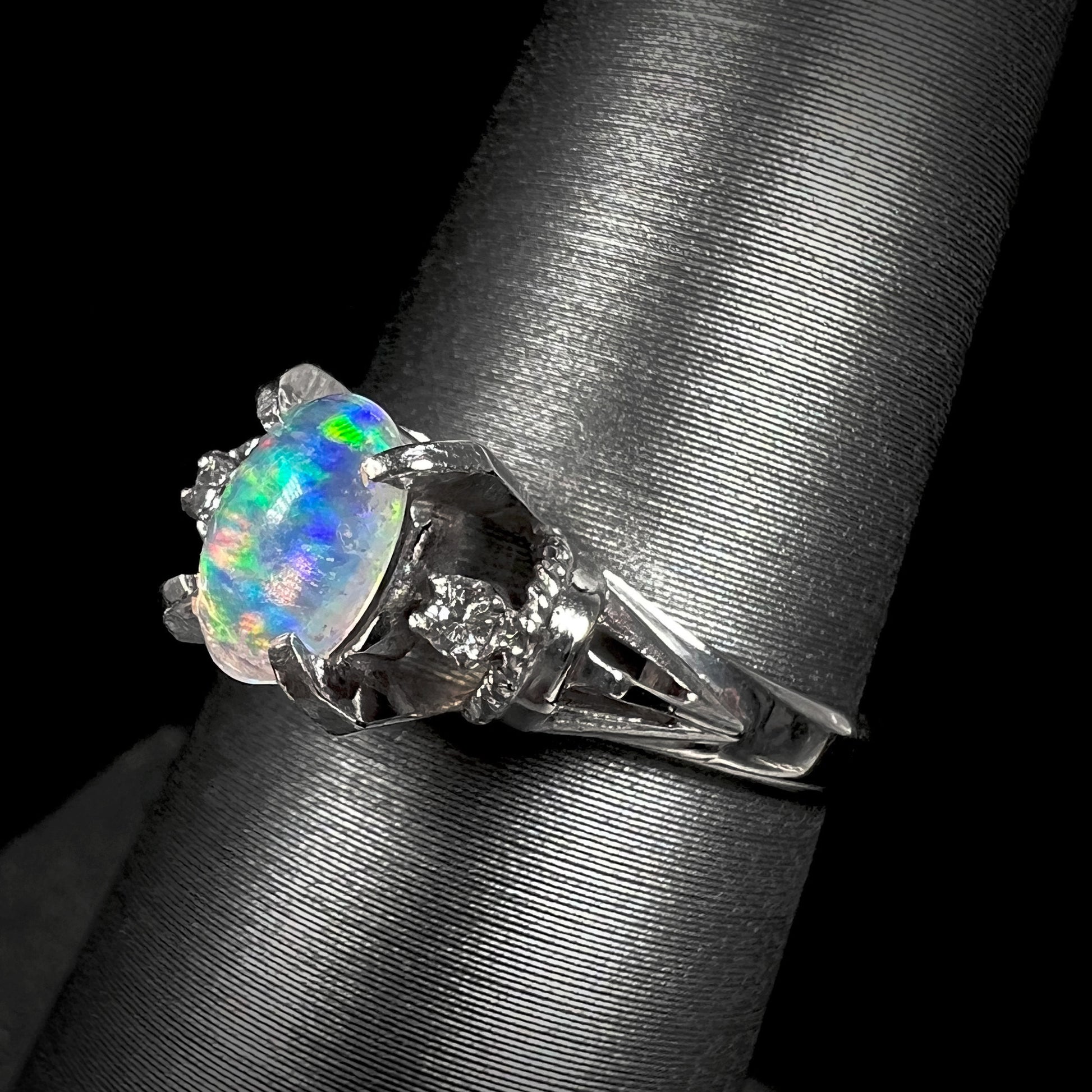 A platinum and diamond-accented jelly opal ring.  The opal shows blue, green, and teal colors.