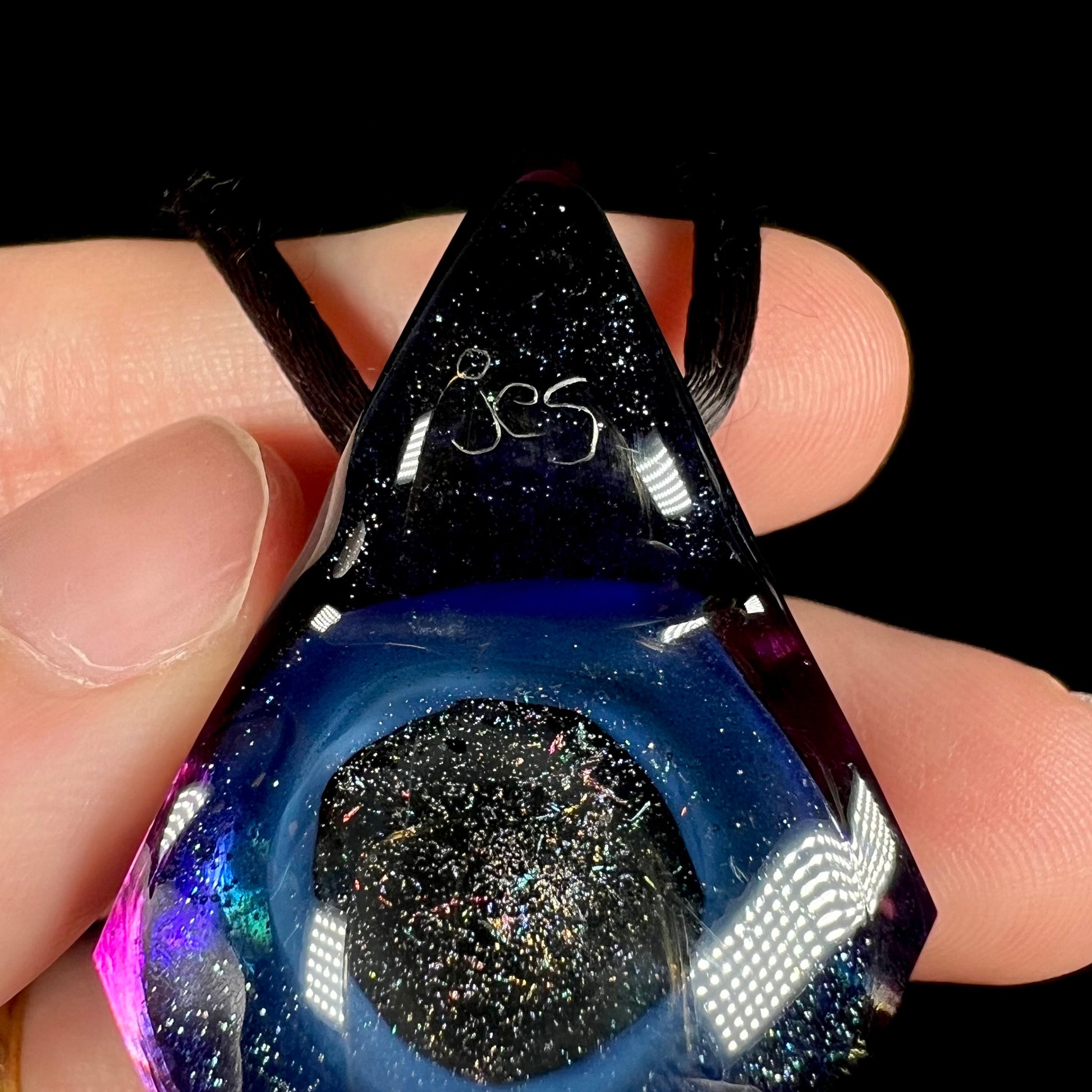 Zoomed in close-up of artist Jes Durfee's signature, "jes", shown etched in the back of a glittery glass pendant.