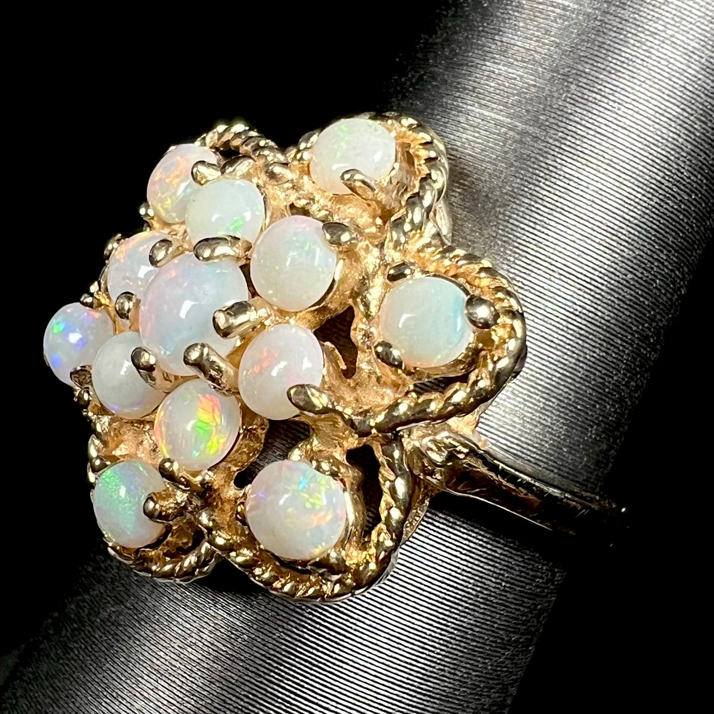 Angled view of a vintage yellow gold atomic-style opal cluster ring made by J.M. Fox, shown on a ring display against a black background.