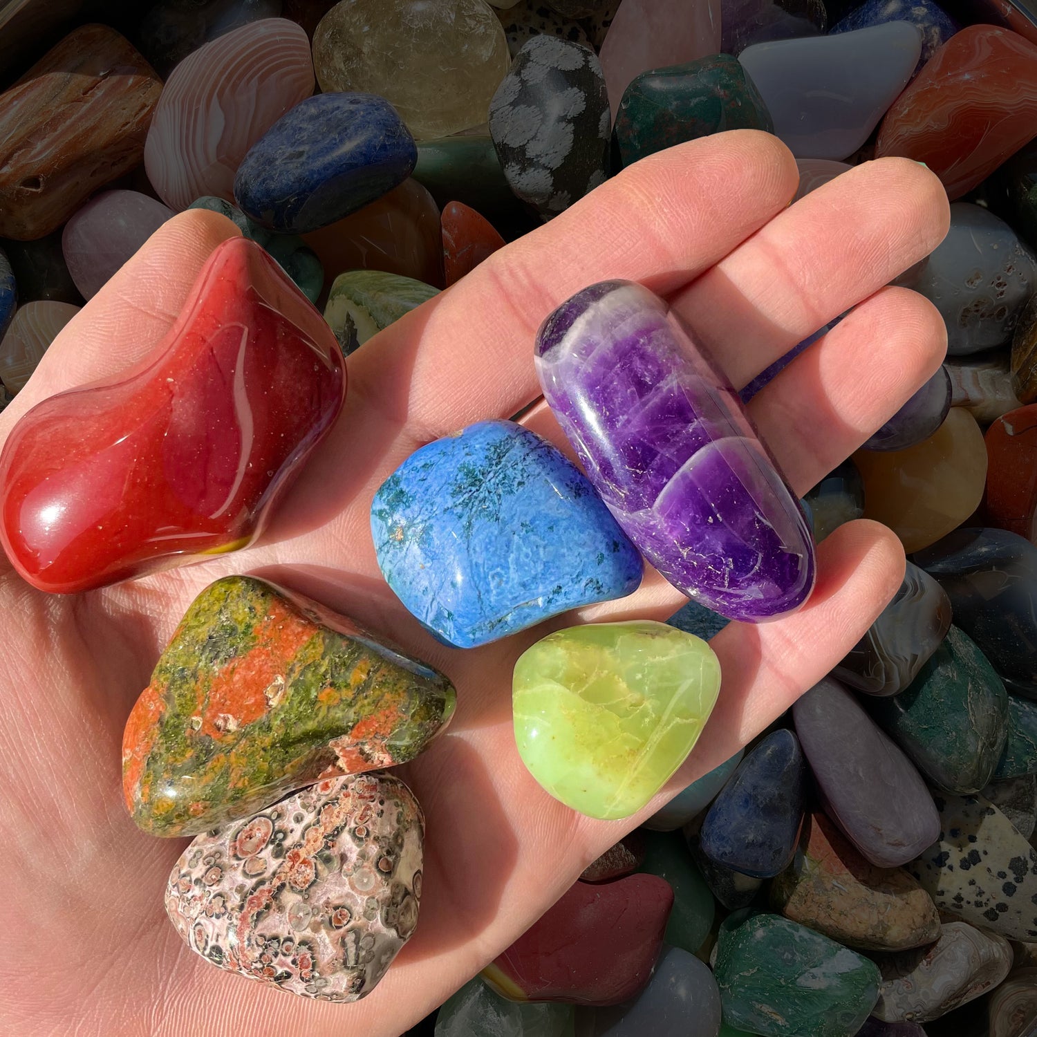 Six extra large tumbled stones are resting on a person's hand.  Stones are roughly the person's thumb in size.