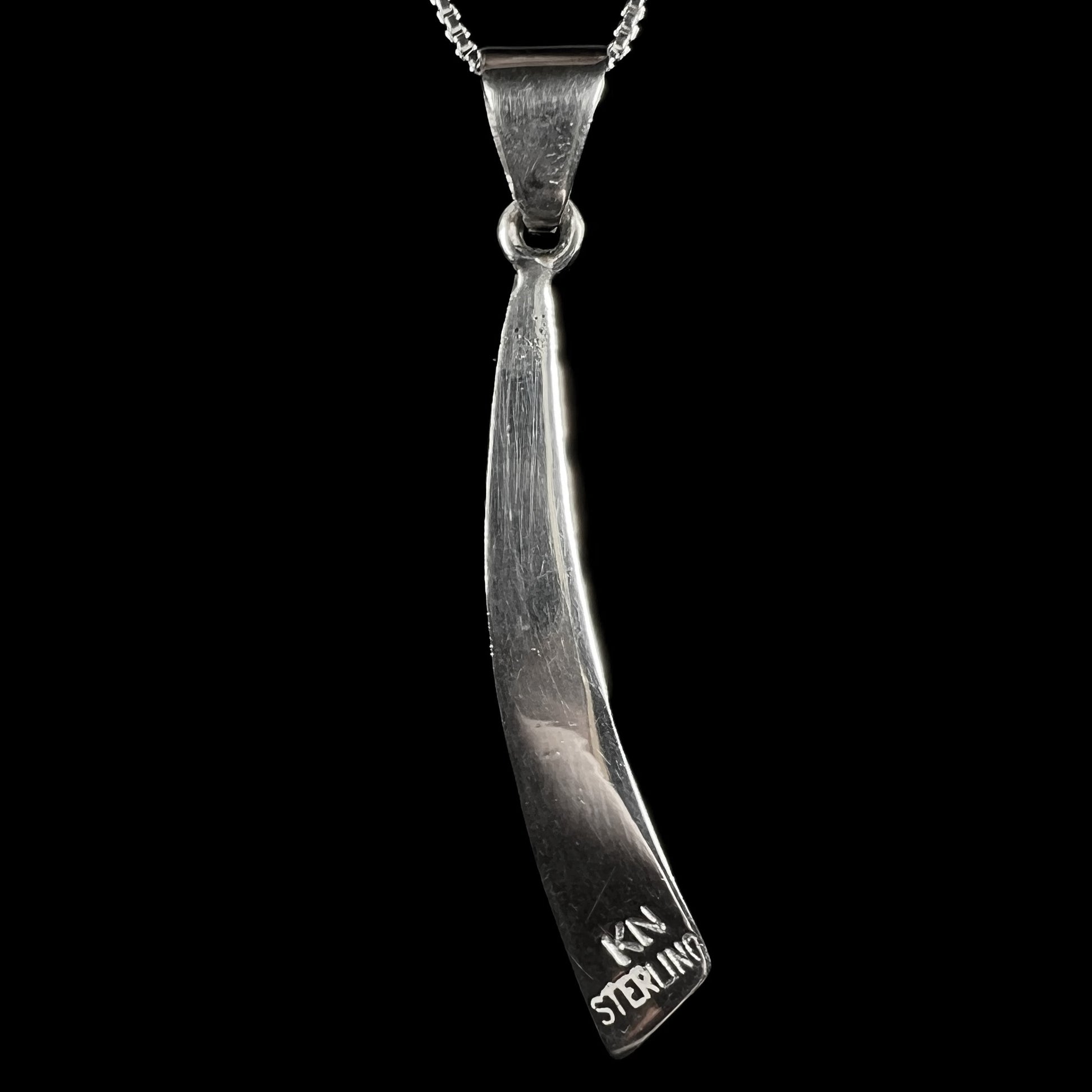 Back side of a sterling silver pendant stamped "KN STERLING" on black background.