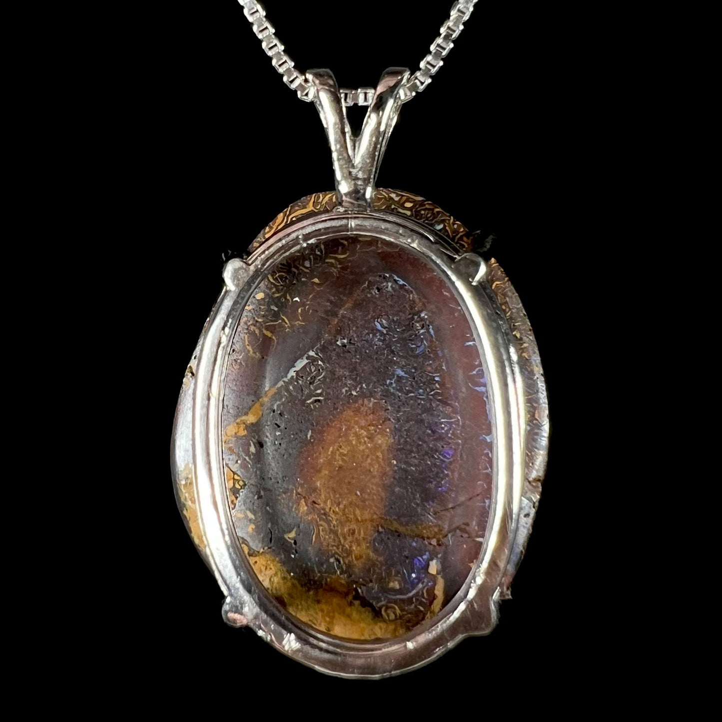 The back of a Koroit boulder opal necklace, revealing its silver-plated basket setting and the natural opal's dark ironstone matrix.