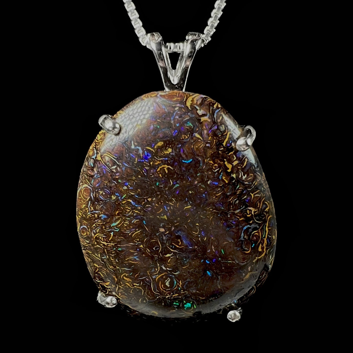 A close-up macro view of a Koroit boulder opal necklace, showcasing its intricate ironstone matrix and blue-green fire, set in a silver-plated basket-style mounting.