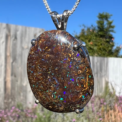 A macro close-up of a Koroit boulder opal necklace in natural sunlight, showing blue and purple flashes against its ironstone background.