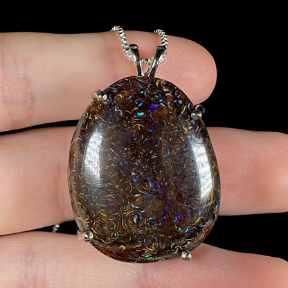 A macro close-up of a Koroit boulder opal necklace resting on fingers, highlighting the opal's intricate ironstone matrix and flashes of color.