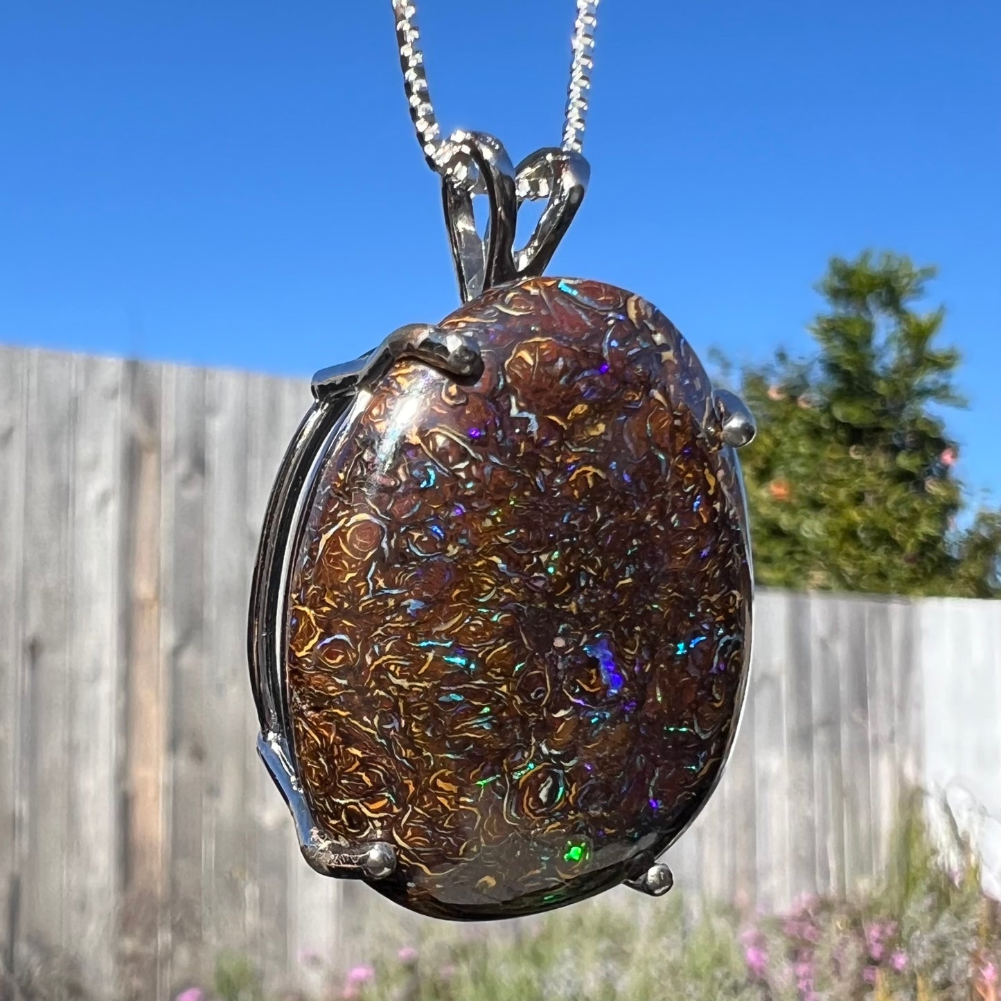 A macro close-up of the opposite side of a Koroit boulder opal necklace in natural sunlight, highlighting its swirling ironstone matrix and natural opal textures.