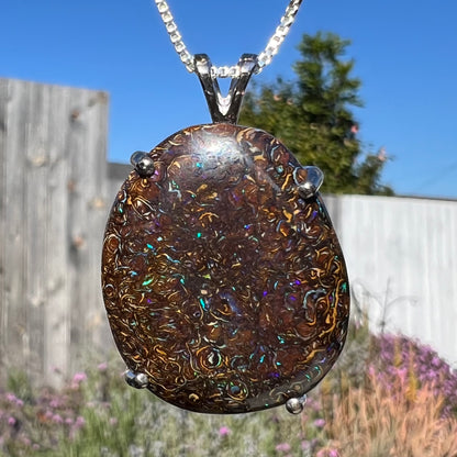 A macro close-up of a Koroit boulder opal necklace dangling in natural light, emphasizing the opal's intricate ironstone patterns and play of color.