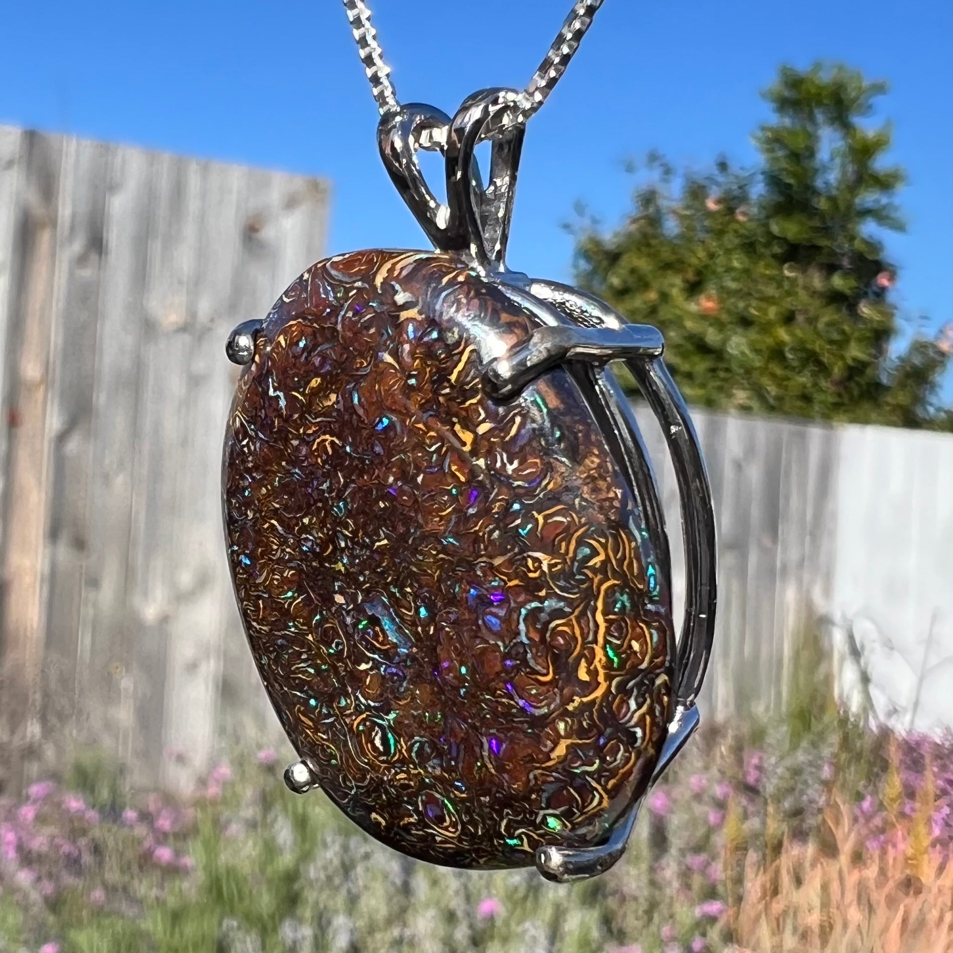 A close-up macro shot of a Koroit boulder opal necklace in natural light, capturing its earthy ironstone patterns with subtle blue flashes.