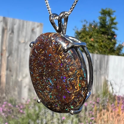 A close-up macro shot of a Koroit boulder opal necklace in natural light, capturing its earthy ironstone patterns with subtle blue flashes.