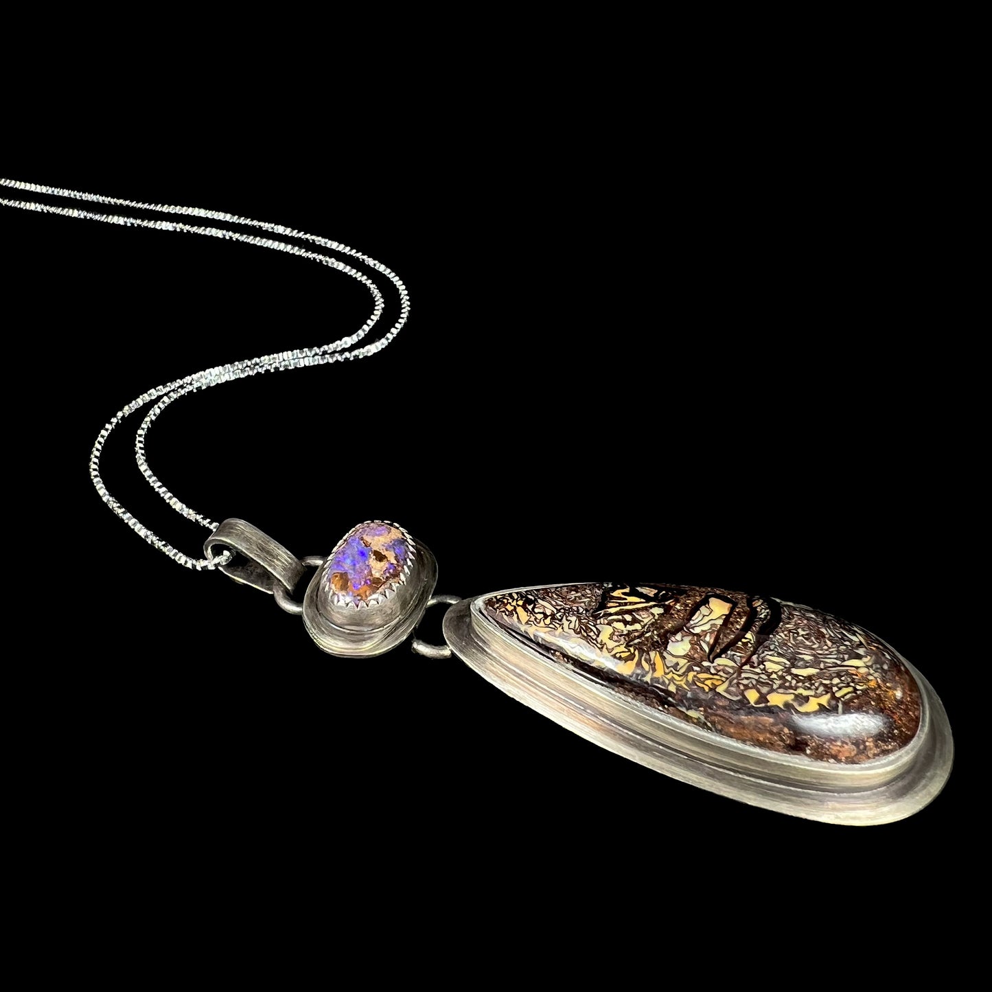 A two-stone Koroit boulder matrix opal necklace by Mer Made Designs shown laying against a black background.
