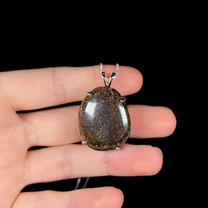 A Koroit boulder opal necklace resting on fingers, showcasing the natural opal's swirling ironstone patterns and subtle blue-green flashes.