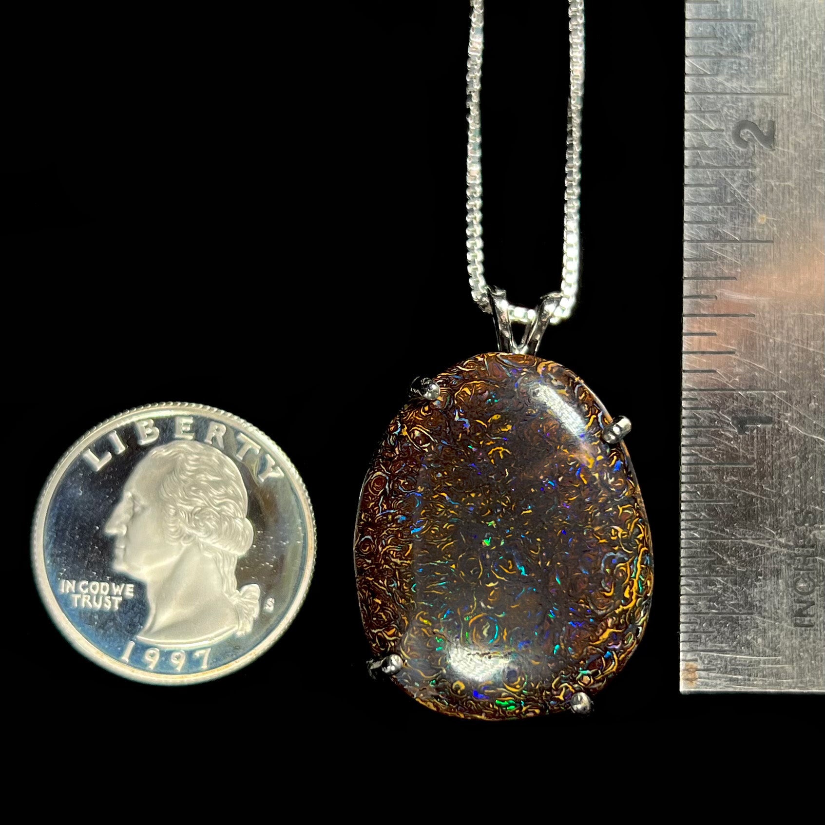 A Koroit boulder opal necklace placed next to a quarter and ruler for size reference, showing its approximately 1-inch pendant.