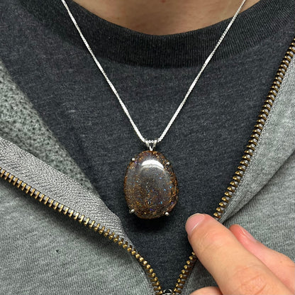 A Koroit boulder opal necklace worn around the neck on a black t-shirt with a partially zipped sweatshirt, showing how it sits when worn.