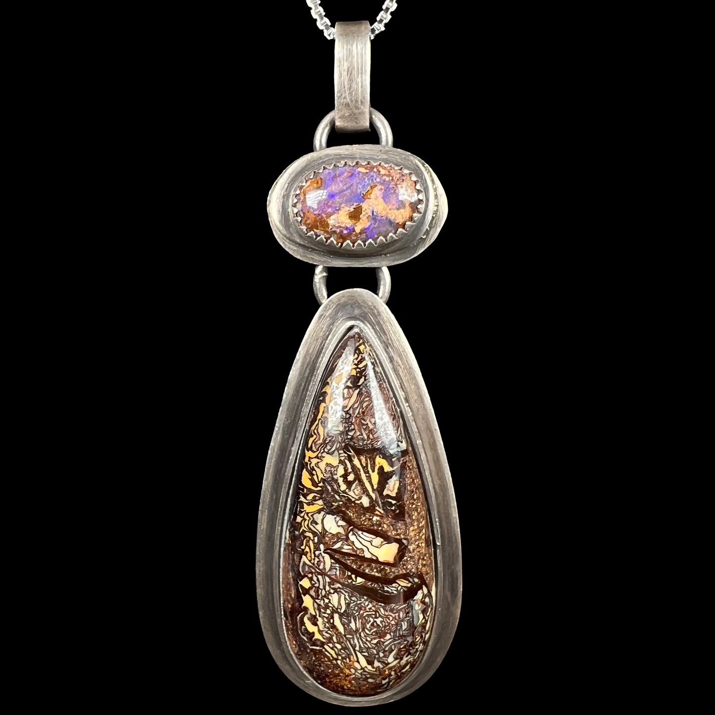 Macro close-up of a rustic sterling silver two-stone Koroit boulder opal pendant by Amy Flanders of Mer Made Designs, shown on black background.