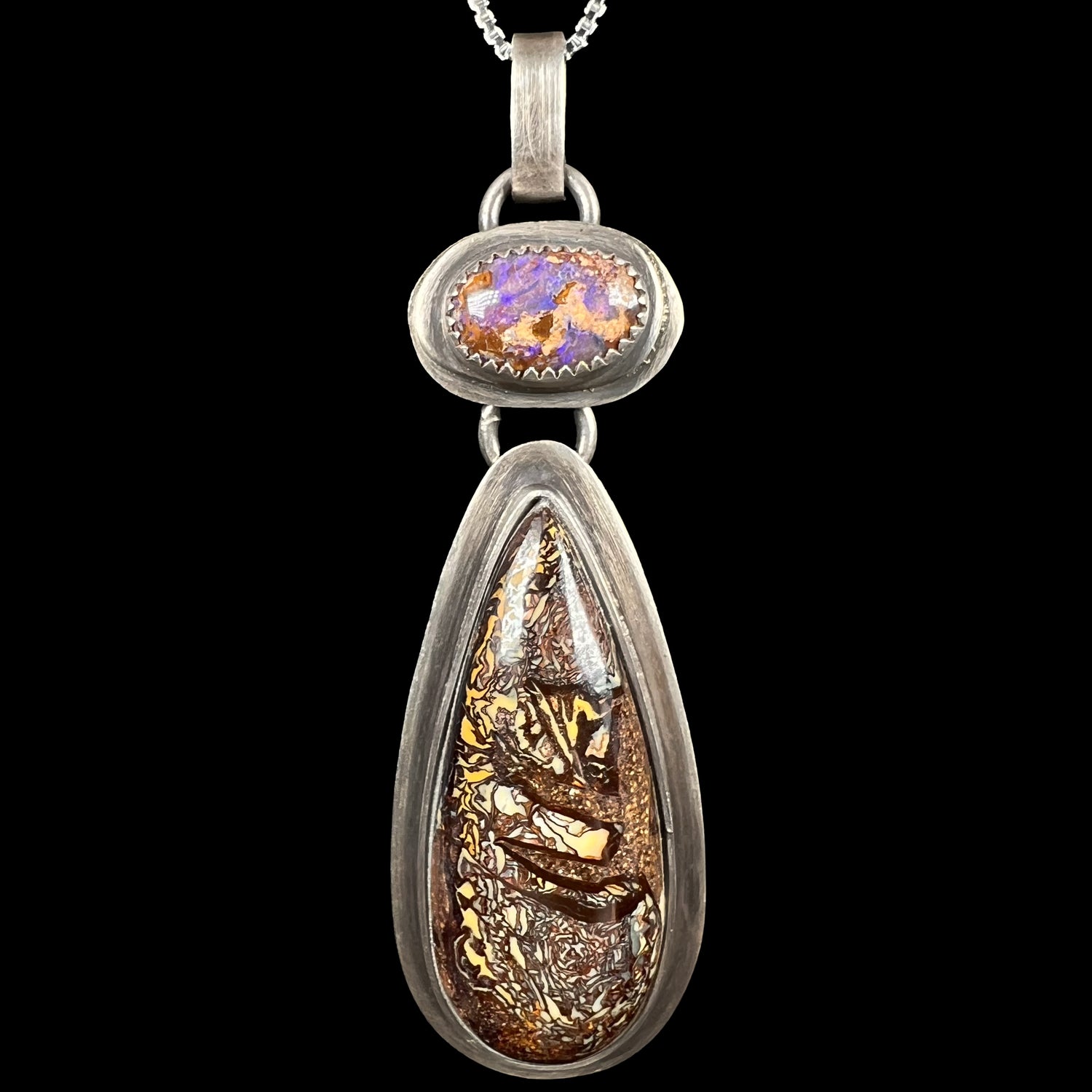 Macro close-up of a rustic sterling silver two-stone Koroit boulder opal pendant by Amy Flanders of Mer Made Designs, shown on black background.