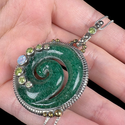 A men's aventurine koru necklace, accented with opal and peridot, shown from an angle in a hand.