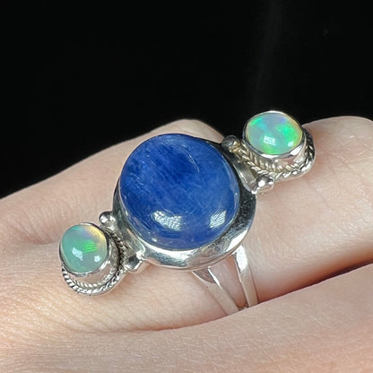 A kyanite and Ethiopian opal-accented ring worn on a finger, shown at an angle against black background.