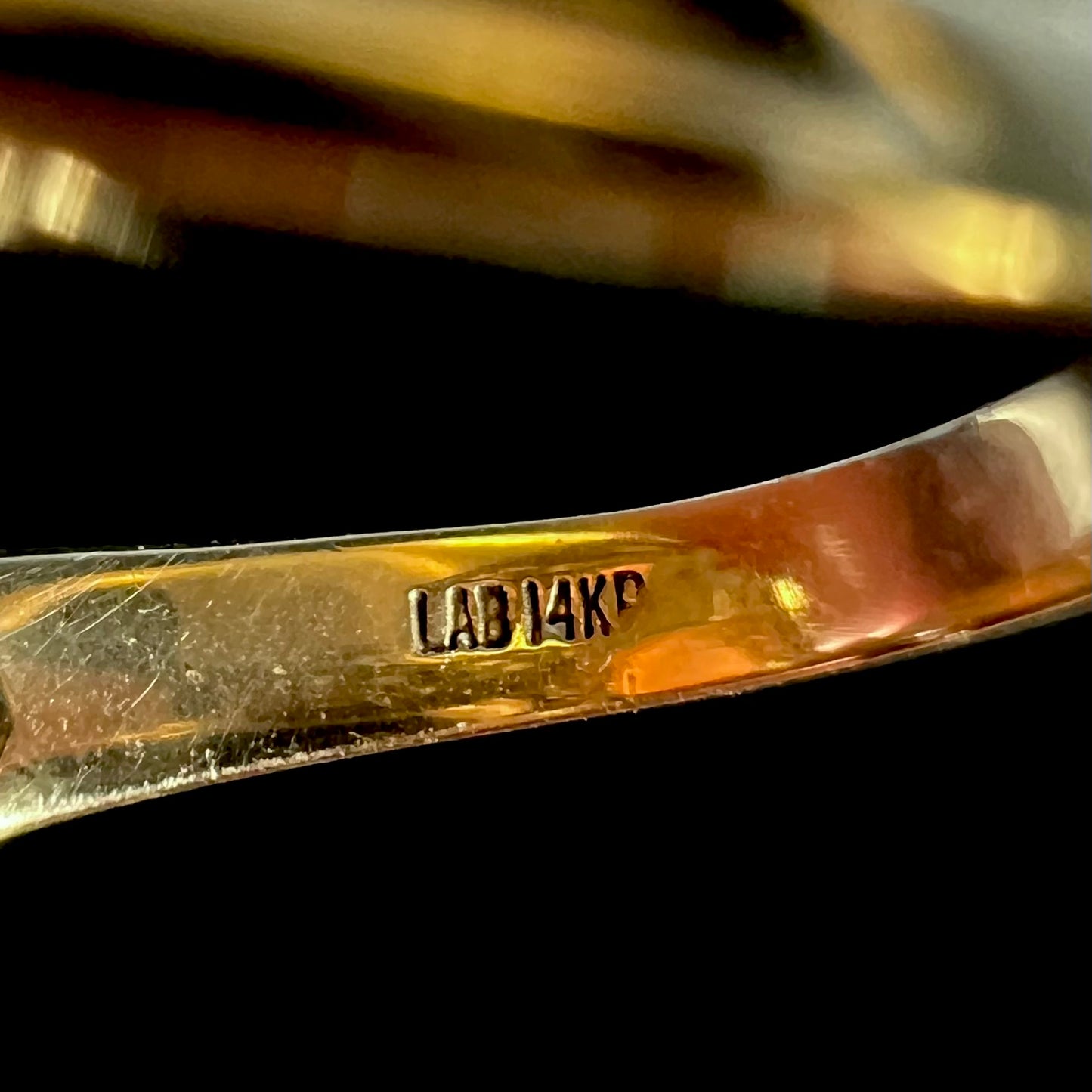 Inside of gold ring's shank, focused on hallmark stamps "LAB" and "14KP", signifiying maker's mark and 14k plumb metal composition.