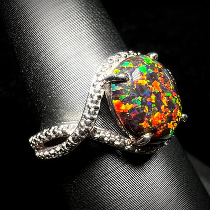 A lab-created black opal solitaire ring with red color play in sterling silver shown at an angle on a ring display.