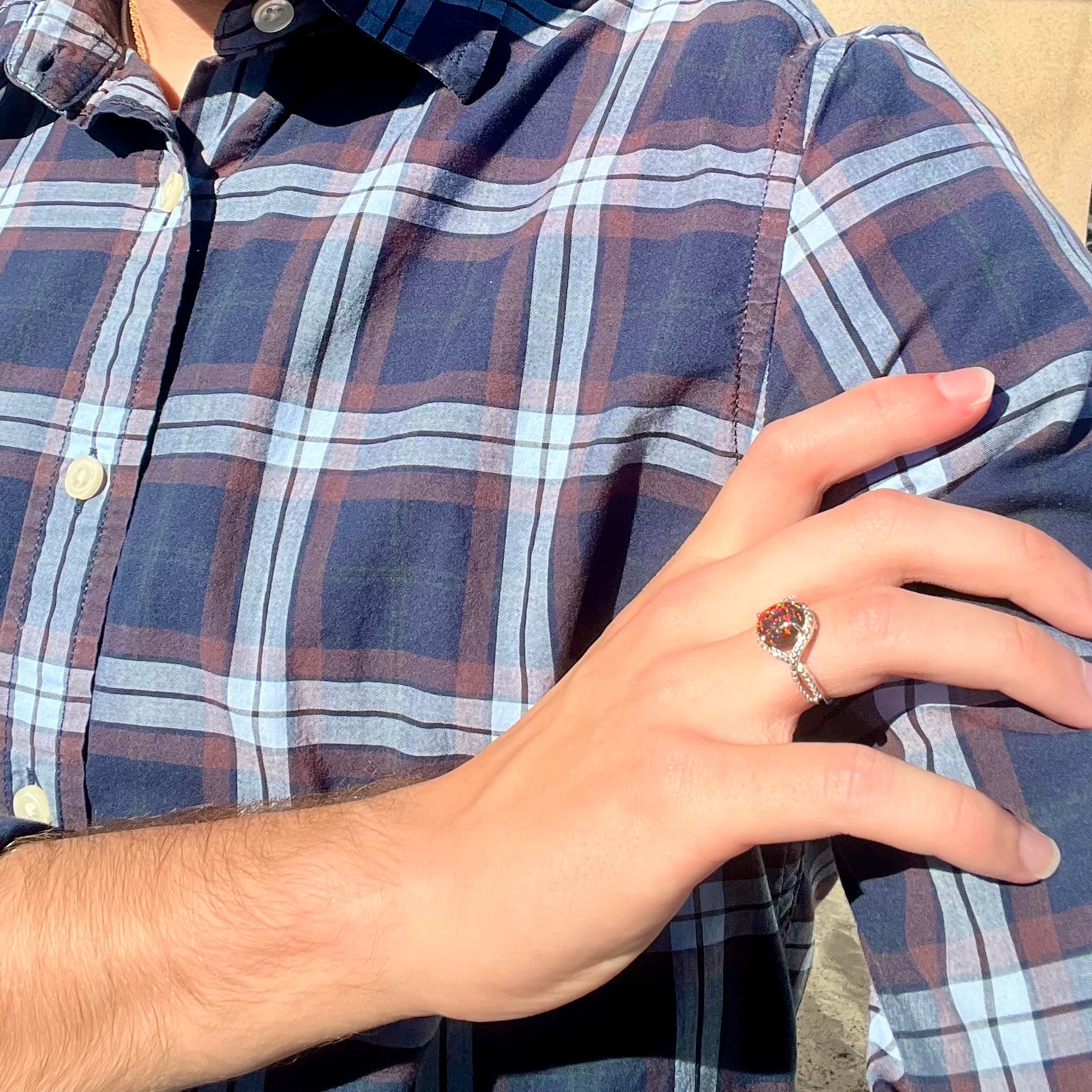 A lab-created black opal solitaire ring with red color play in sterling silver, worn on a hand resting on the model's shoulder.