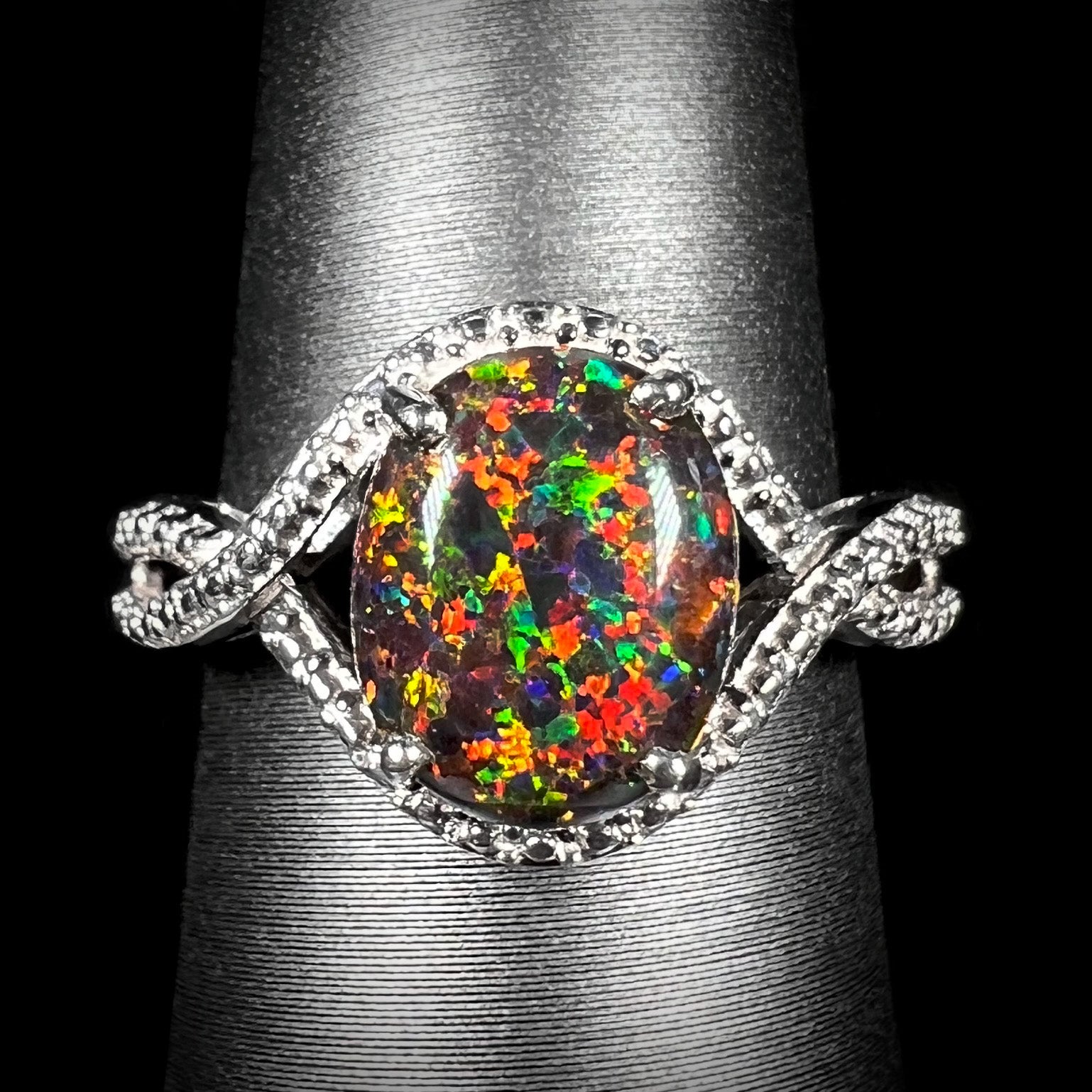 A lab-created black opal solitaire ring with red color play in sterling silver, shown from the front on a ring display.