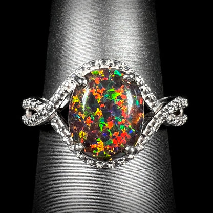 A lab-created black opal solitaire ring with red color play in sterling silver, shown from the front on a ring display.