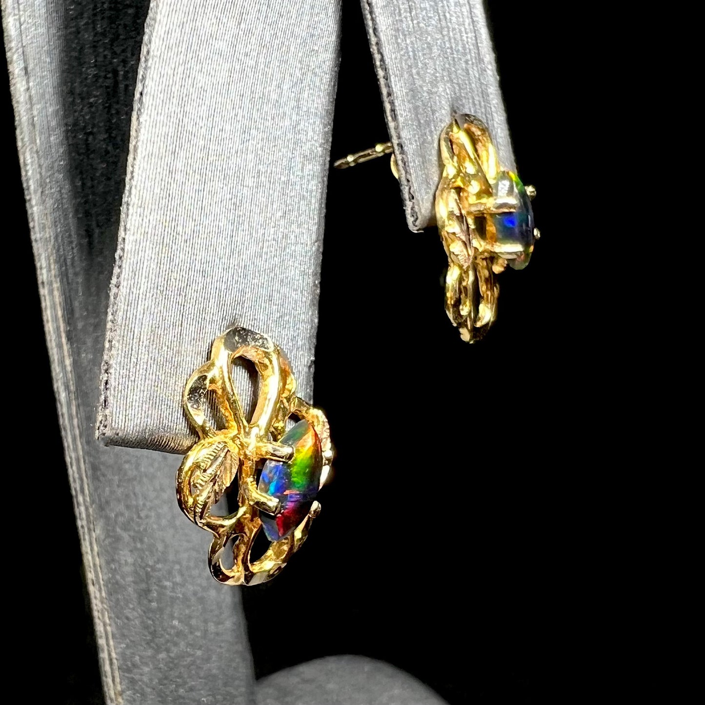 Pair of multicolor lab-created black opal Black Hills gold stud earrings with grape leaf motif on display