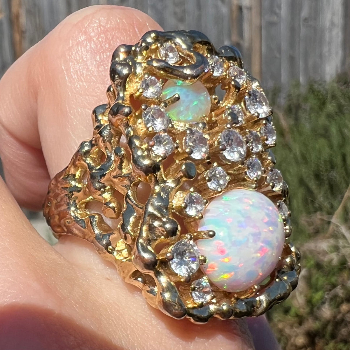 Close-up of a lab-created opal and CZ's statement men's ring worn on finger in sunlight, shown from angle.