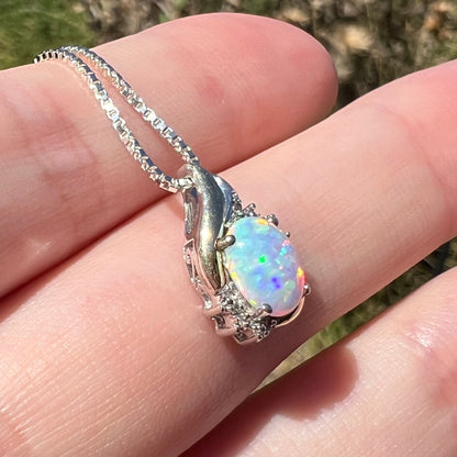 Angled close-up of a lab-created opal and diamond pendant in 10k gold and sterling silver, shown in sunlight.