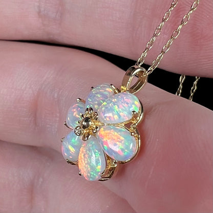 A lab-created opal flower pendant in 14k gold on a dainty gold chain, shown from the side view close-up in a hand