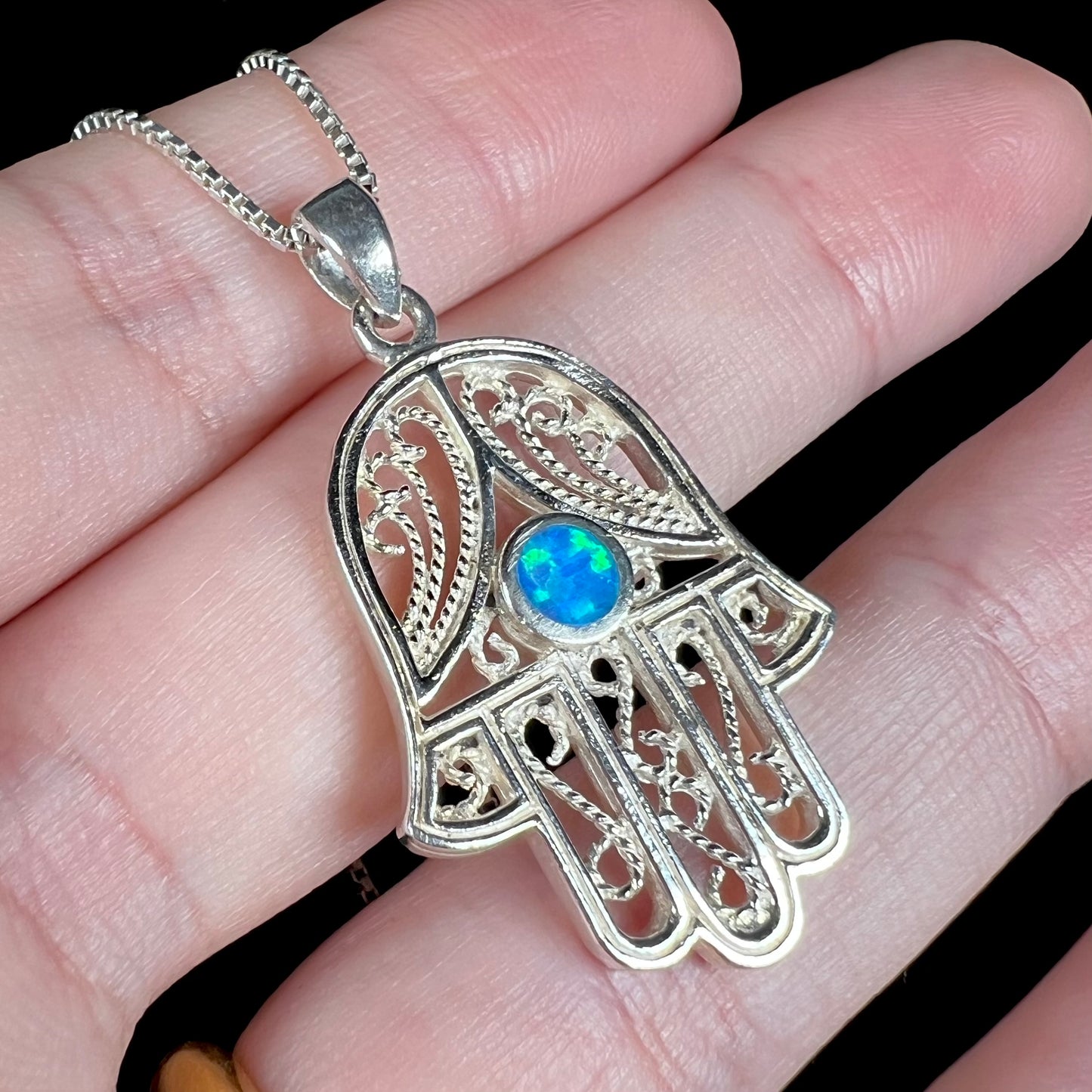 A sterling silver and filigree-accented hamsa hand necklace set with a round lab-created opal.
