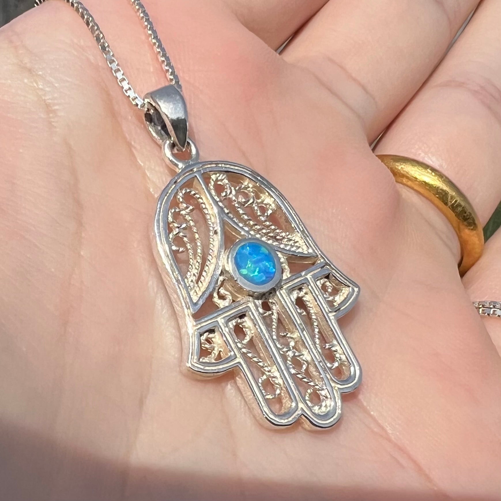 A sterling silver and filigree-accented hamsa hand necklace set with a round lab-created opal.