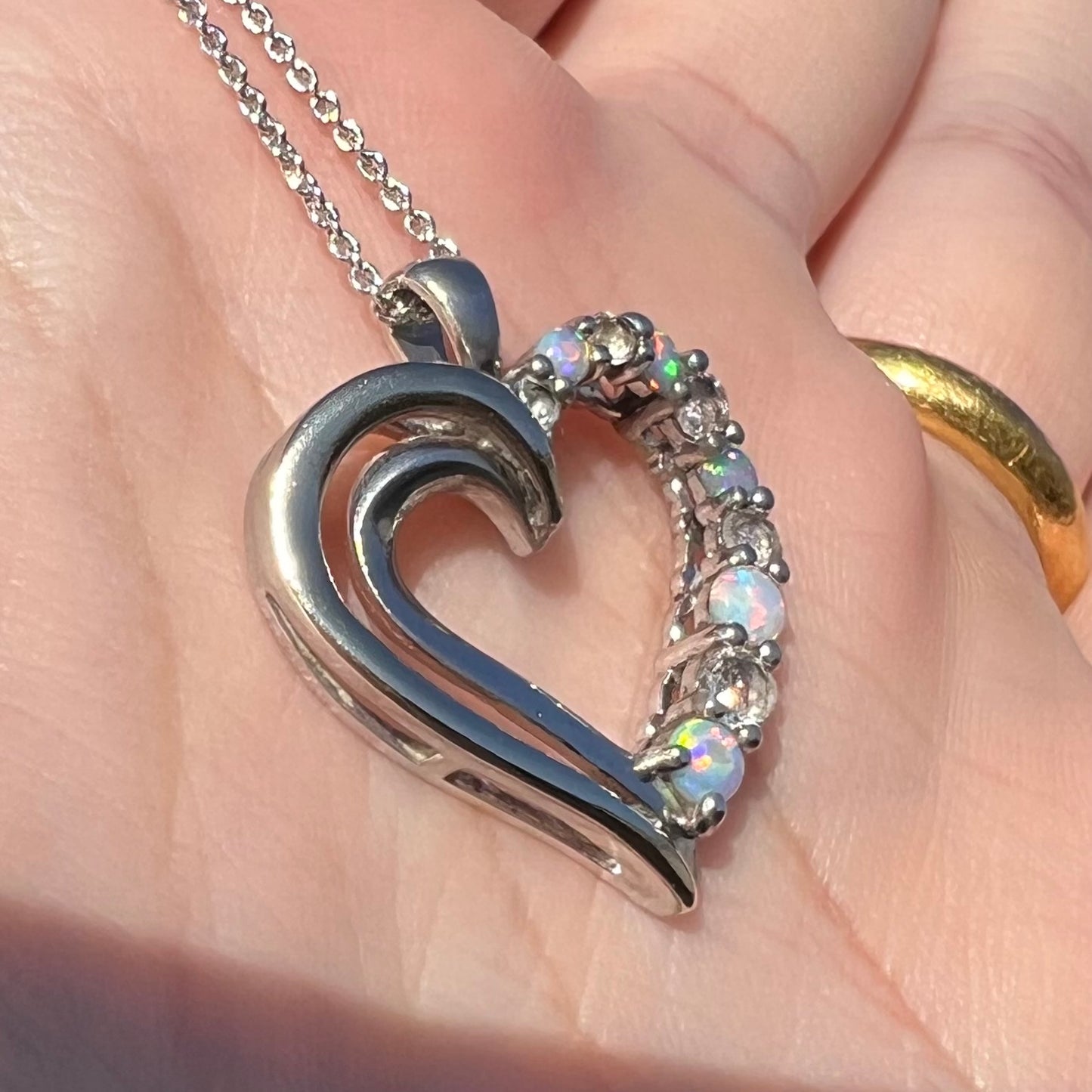Angled sunlit view of a two-tone sterling silver and yellow gold lab-created opal and CZ heart necklace.