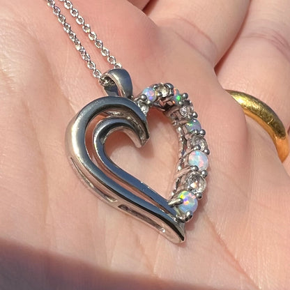 Angled sunlit view of a two-tone sterling silver and yellow gold lab-created opal and CZ heart necklace.