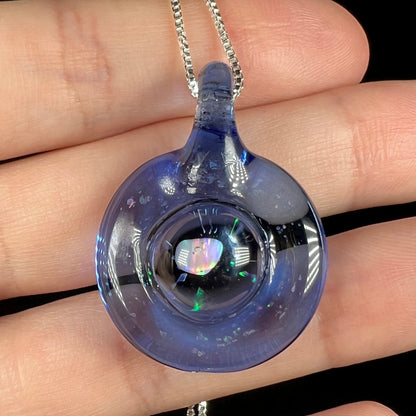 Close-up of a hand holding a lab-created opal in blue glass pendant by Michigan artist, Cameron Scott.