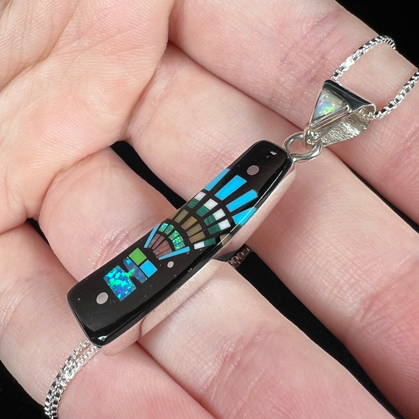 Lab-created opal and black onyx inlay pendant with Southwest-style motif shown close-up from angle held in hand.