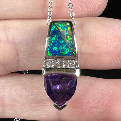 Macro close-up of lab-created opal inlay and purple trillion cut CZ pendant made from sterling silver, resting on fingers.