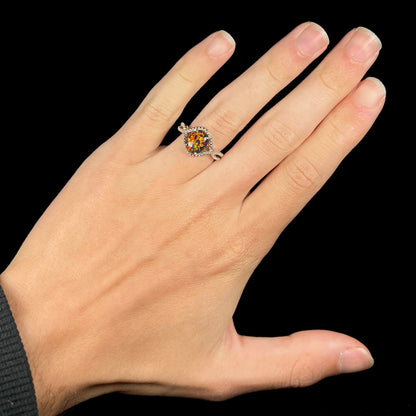 A lab-created black opal solitaire ring with red color play in sterling silver, worn on a hand against black backdrop.